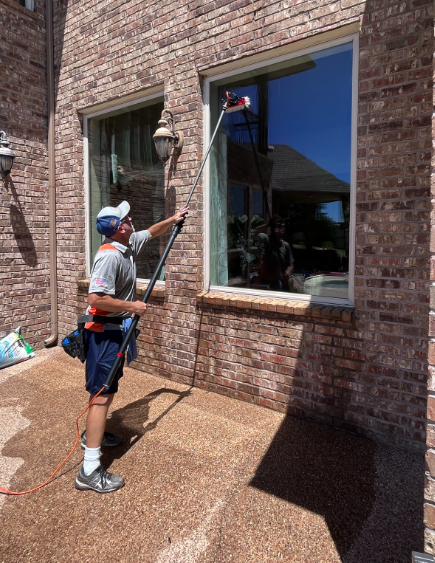 Hartmann window cleaning technician using a high-reach extension pole to safely wash a large exterior home window.