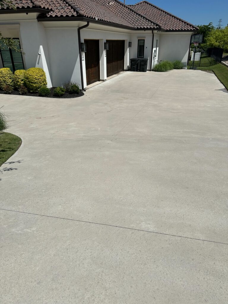 A wide, clean concrete driveway leading up to a house after a professional pressure washing service by Hartmann.