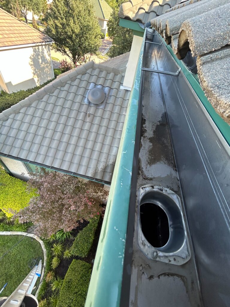 A top-down view of a completely cleaned and cleared residential rain gutter and downspout opening after a professional gutter cleaning service by Hartmann.